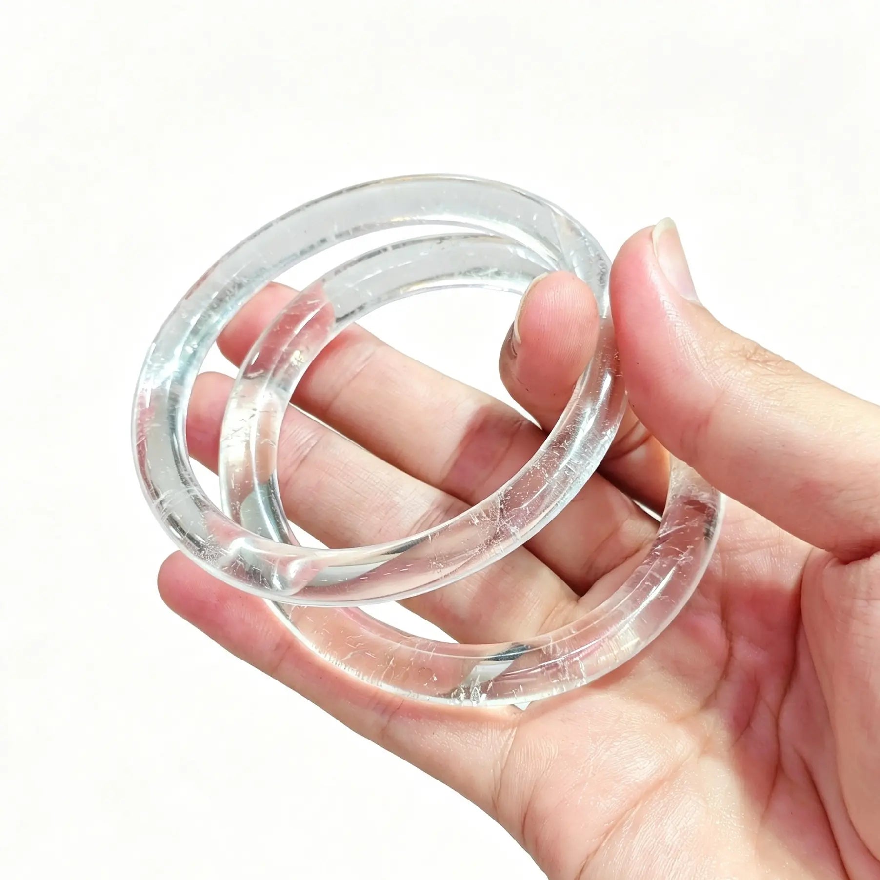 Hand holding a pair of natural clear quartz slim bangles showcasing high icy transparency and glossy finish