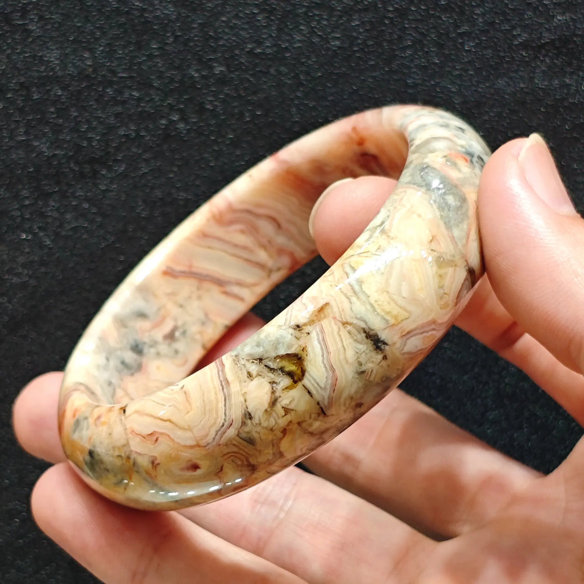 hand holding genuine crazy lace agate bangle showing warm swirling bands
