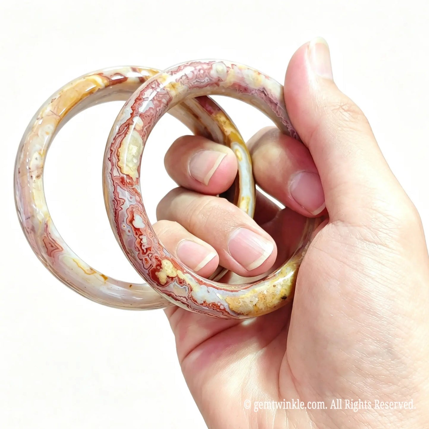 Hand displaying two natural crazy lace agate bangles showing polished mineral swirls