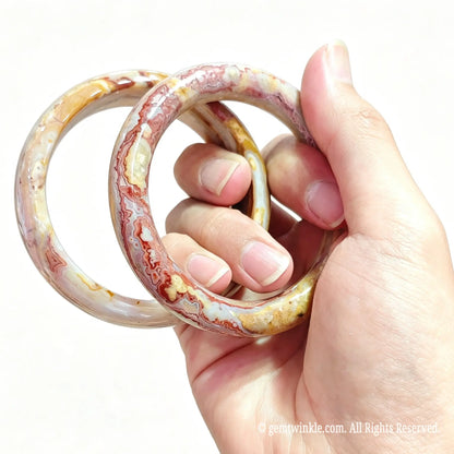 Hand displaying two natural crazy lace agate bangles showing polished mineral swirls