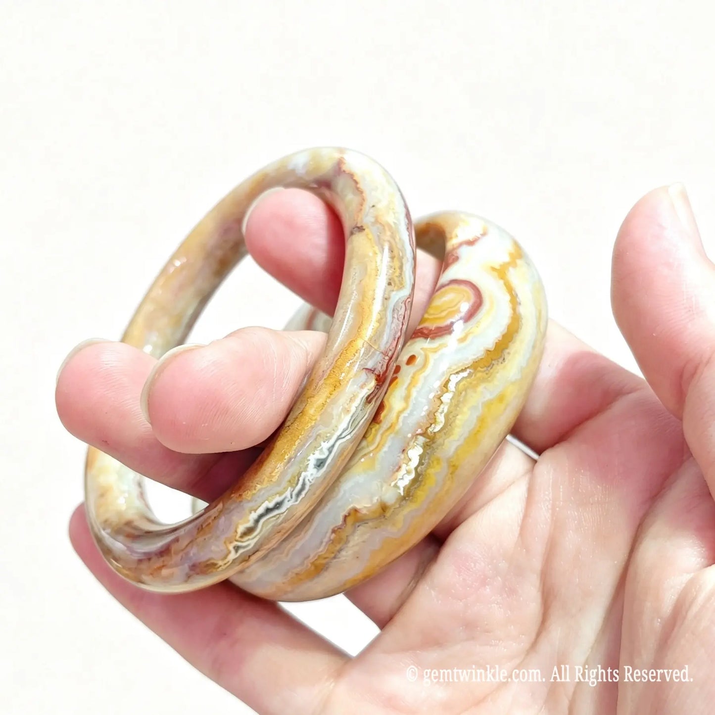 Pair of natural crazy lace agate bangles held in hand showing warm earth tone banding