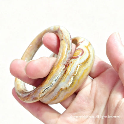 Pair of natural crazy lace agate bangles held in hand showing warm earth tone banding