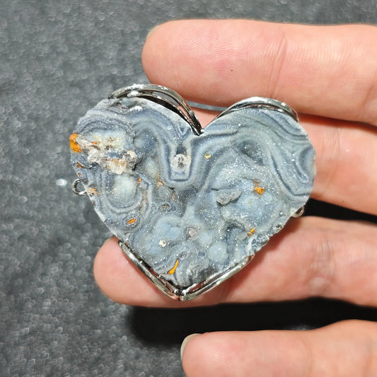 natural crazy lace agate heart pendant displaying grey blue swirling lace bands and sparkling micro druzy center held in a metal frame