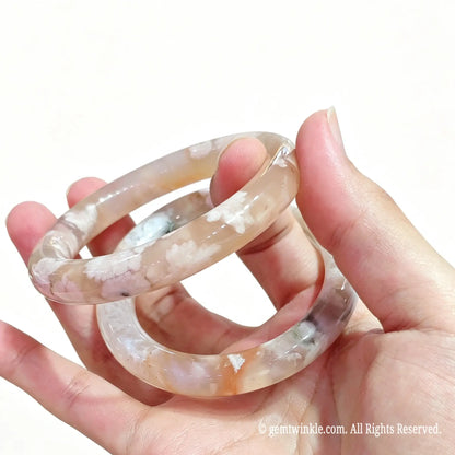 Side view of polished natural flower agate bangle displaying glossy surface luster and soft blush undertones