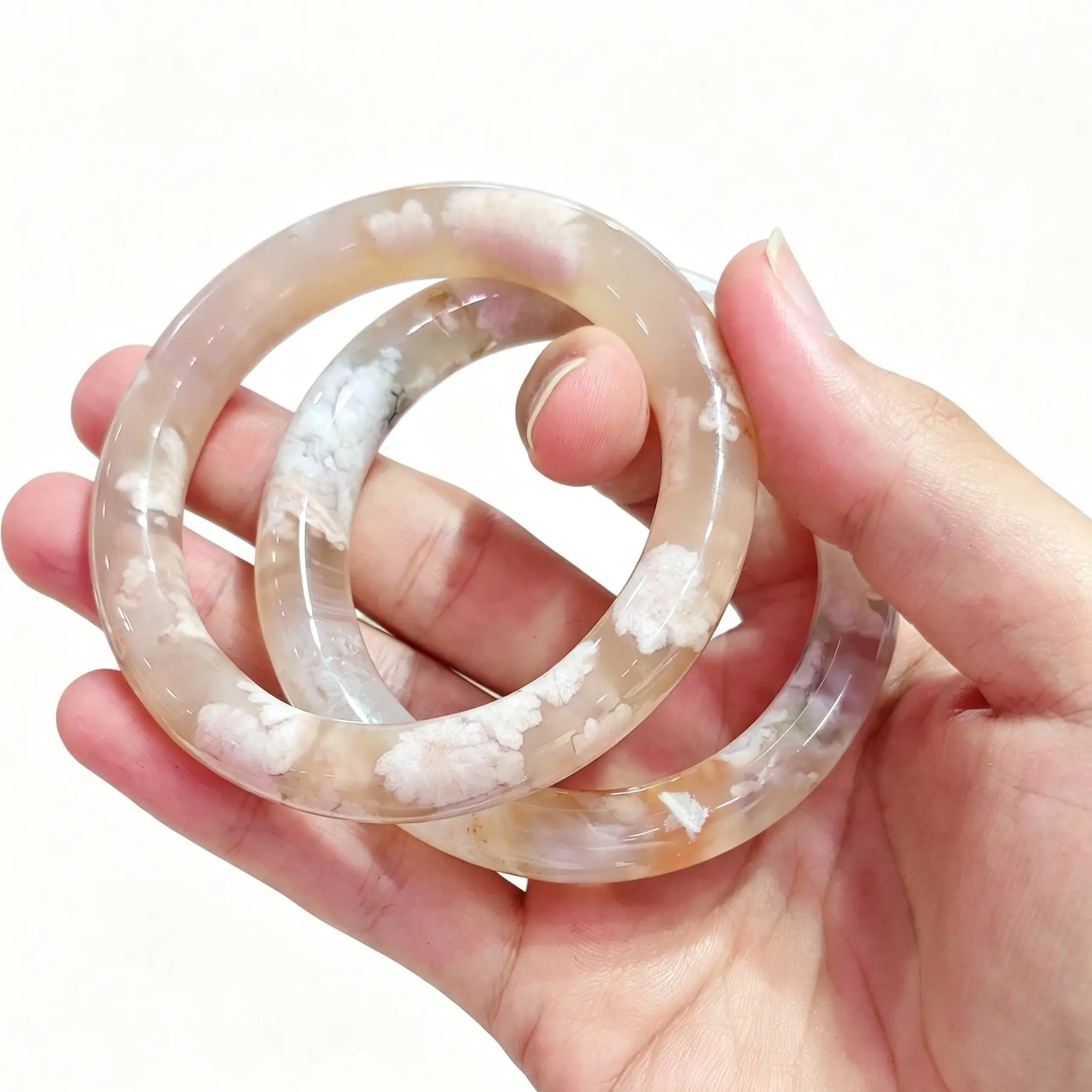 Hand holding a pair of natural cherry blossom agate bangles showcasing translucent chalcedony and floral inclusions
