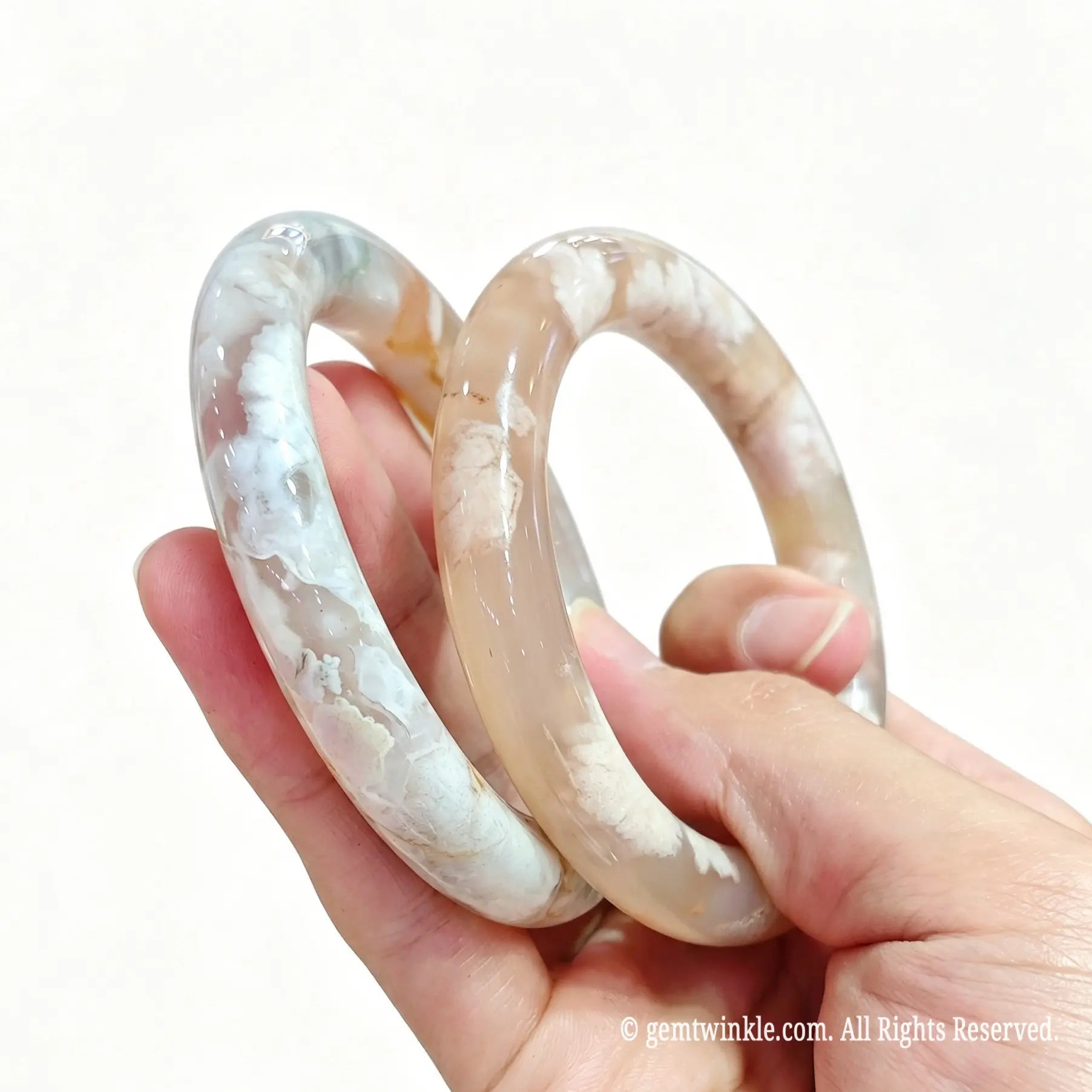 Hand displaying a pair of polished natural cherry blossom agate bangles for small shop inventory