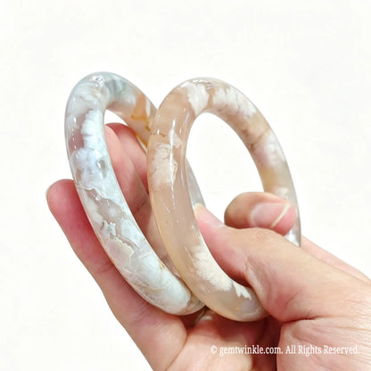 Hand displaying a pair of polished natural cherry blossom agate bangles for small shop inventory