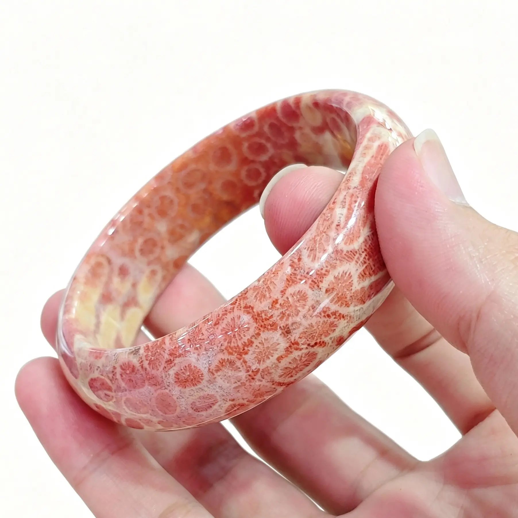 Hand holding a natural fossil coral agate bangle showing distinct pinkish orange chrysanthemum patterns