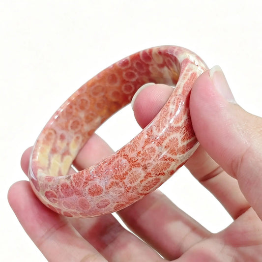 Hand holding a natural fossil coral agate bangle showing distinct pinkish orange chrysanthemum patterns