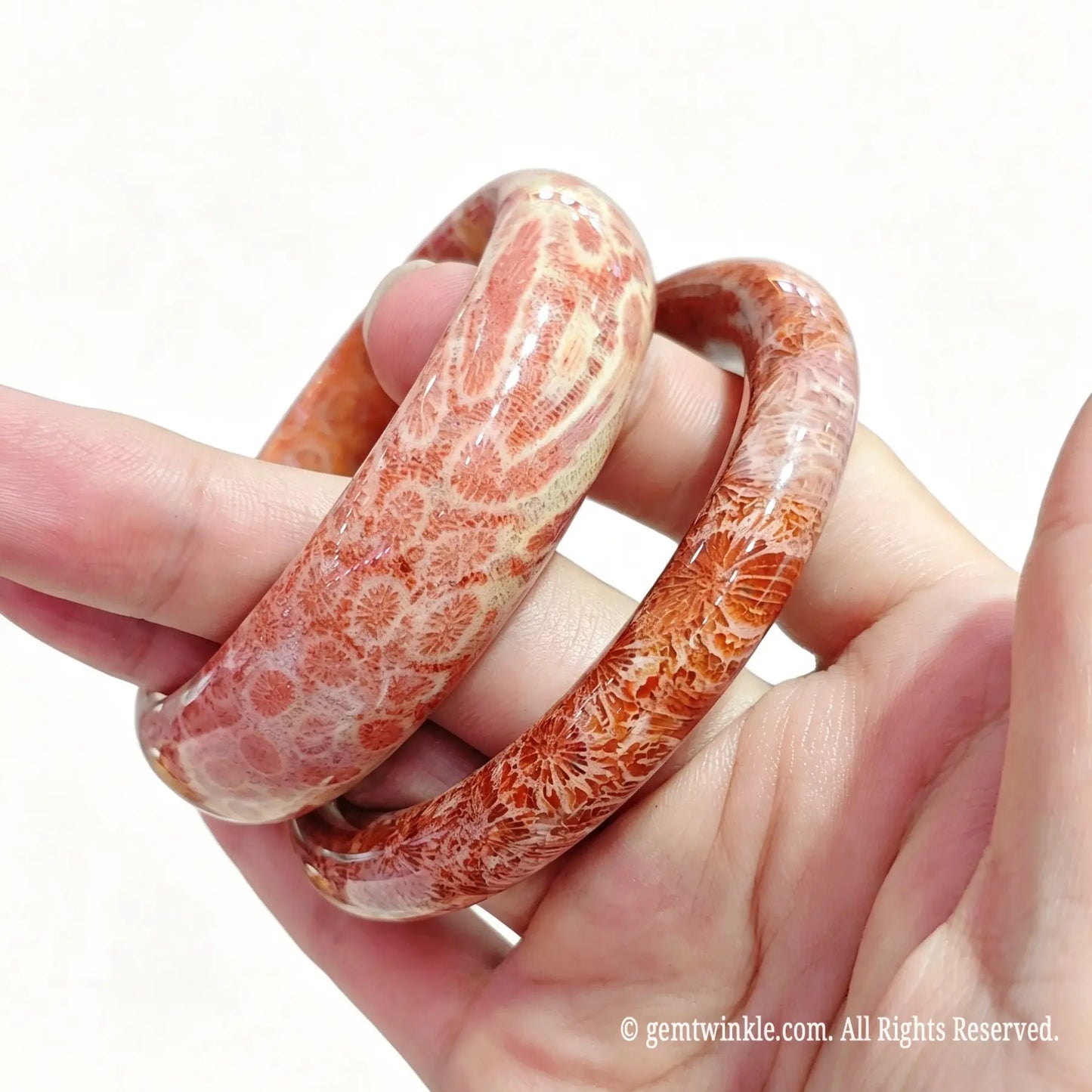 Hand displaying two natural fossil coral bangles with rich orange pink flower pattern details