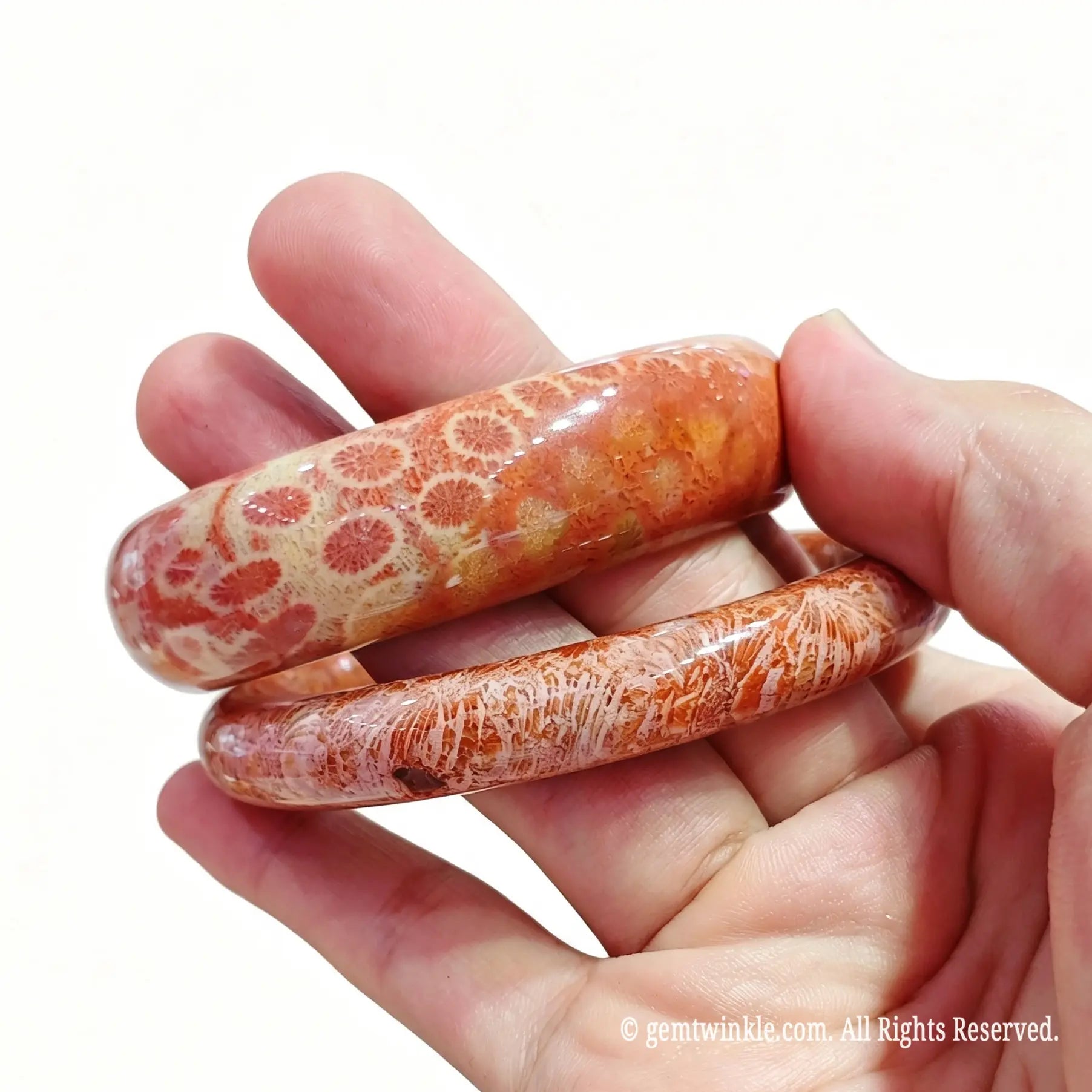 Pair of natural fossil coral agate bangles held in hand displaying warm floral cell patterns