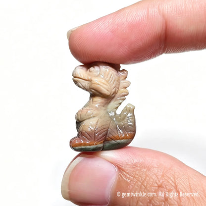 Side view of a mini hand-carved Alashan agate baby T-Rex figurine held between fingers showing detailed spine carving
