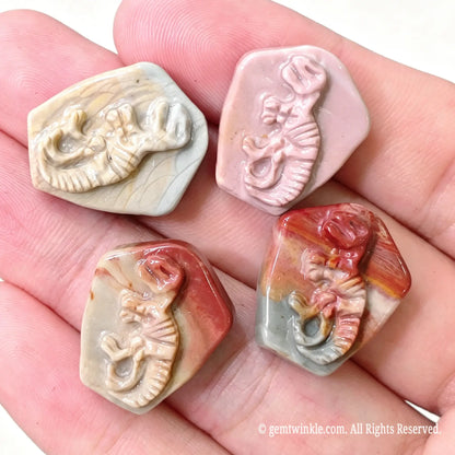 Four carved Alashan agate T-Rex dinosaur fossil relief stones held in hand showing natural color variations