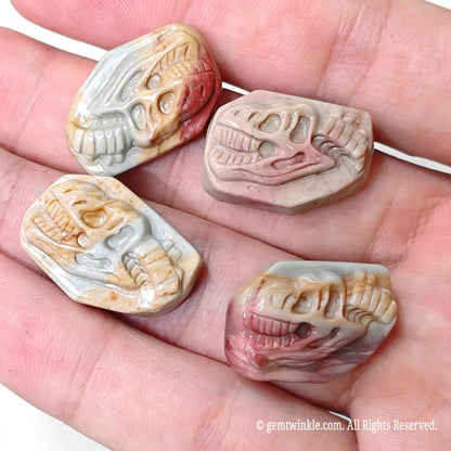 Four carved Alashan agate T-Rex dinosaur skull stones held in hand showing natural mineral color variations