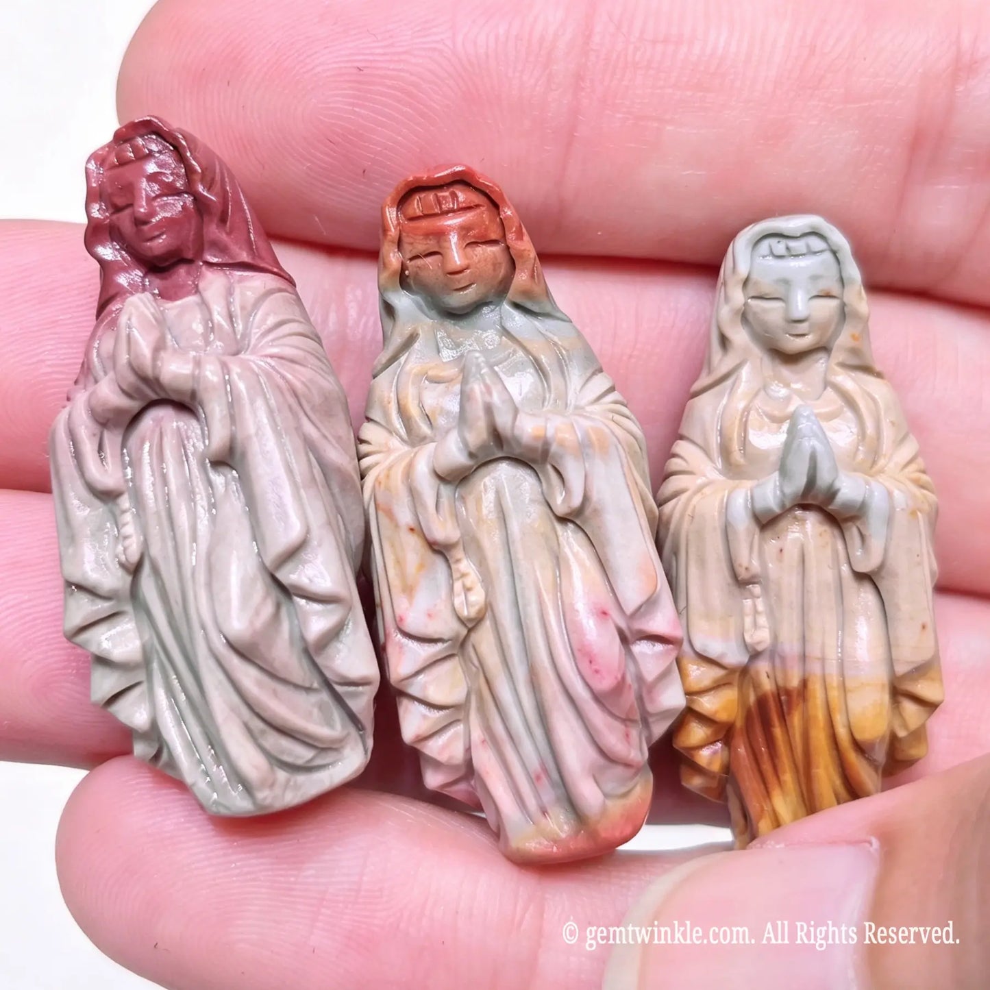 Three hand-carved Alashan agate Virgin Mary statues held in hand displaying natural color variations