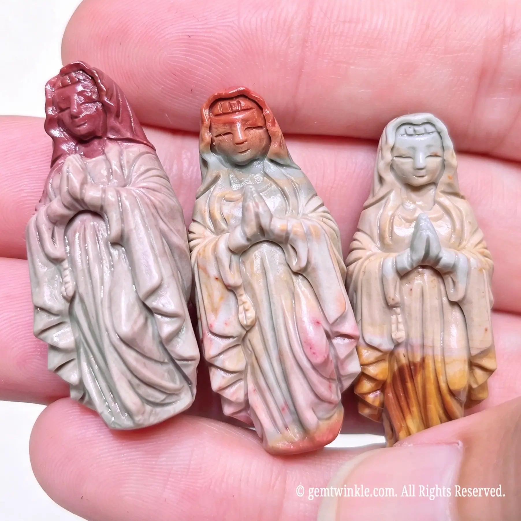 Three hand-carved Alashan agate Virgin Mary statues held in hand displaying natural color variations