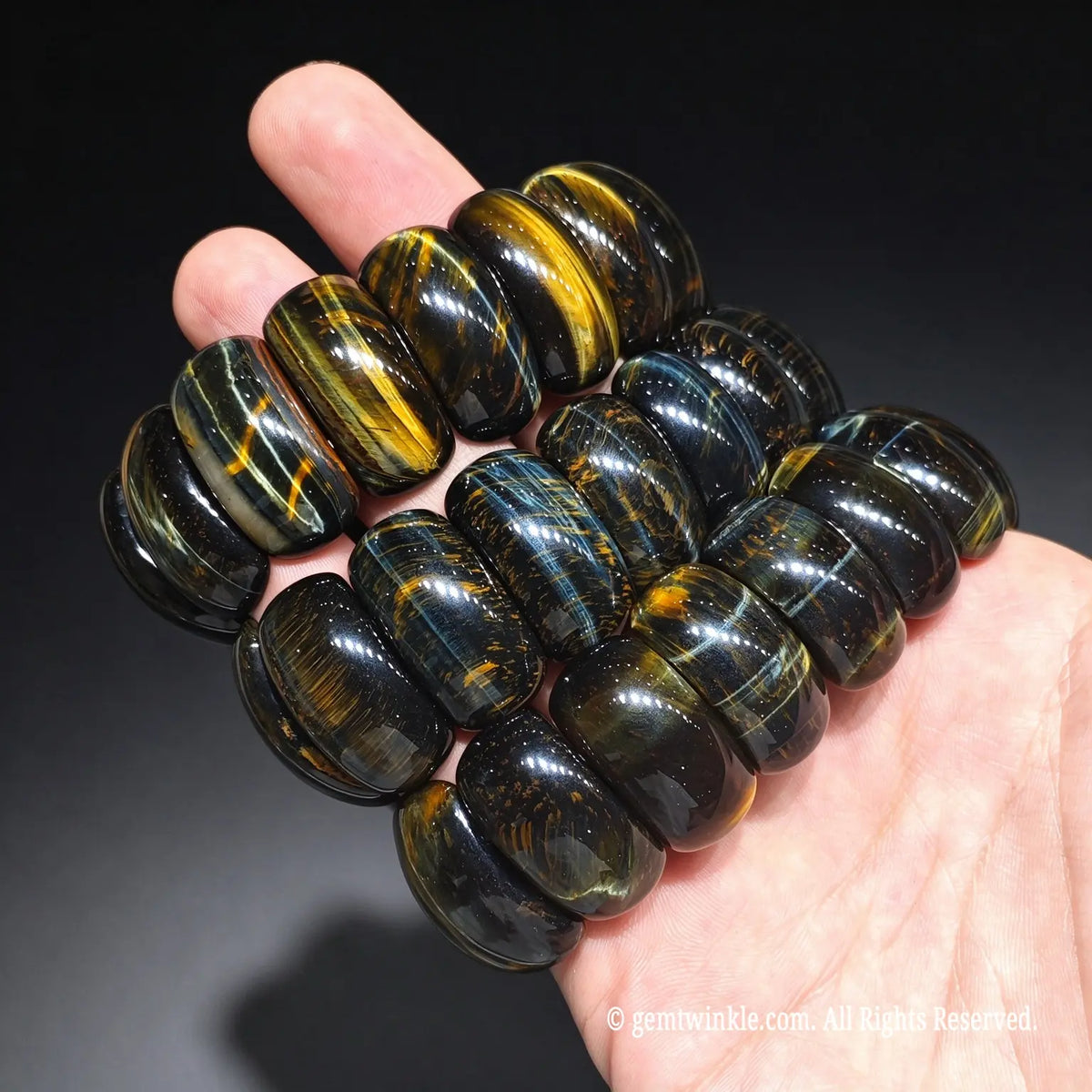 group of natural gold and blue tiger eye barrel bead stretch bracelets held in hand showing strong chatoyant silky sheen
