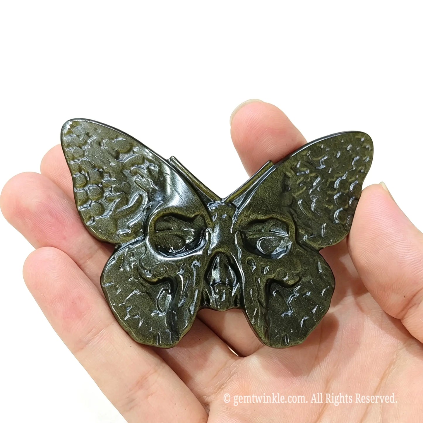 Hand holding natural golden obsidian gothic butterfly skull figurine highlighting size and golden metallic luster