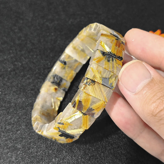 natural golden rutilated quartz plate bracelet held in hand showcasing metallic rutile inclusions