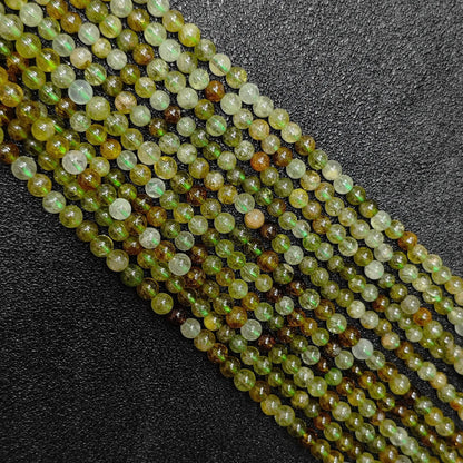 close up diagonal view of 3mm natural green garnet crystal beads loose strands on black background