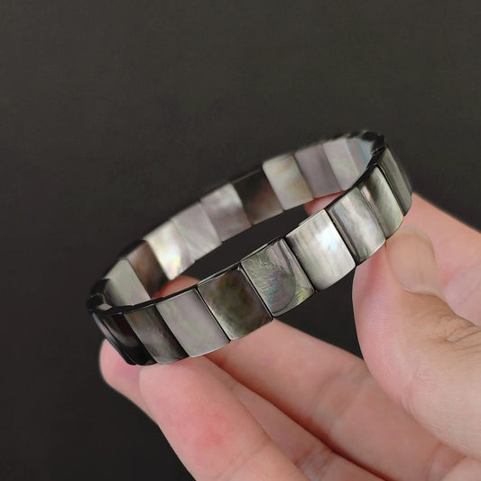 Fingers holding a sleek natural grey mother of pearl stretch bar bracelet featuring rectangular links with silvery iridescence