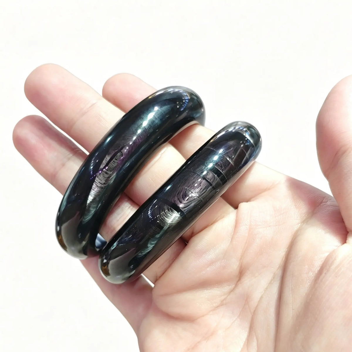 Natural hypersthene bangle bracelet held in hand showing deep black color and silver metallic chatoyancy