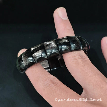 Natural hypersthene block bracelet held in hand under studio lighting showing velvet chatoyant optical flash