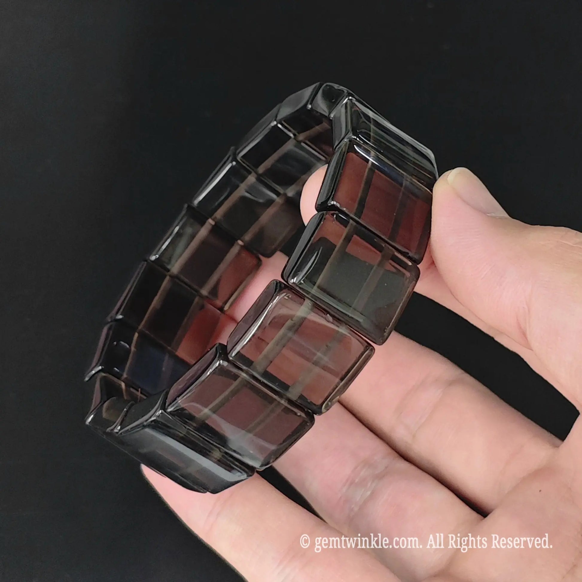 Angle view of natural ice obsidian rectangular plate bead bracelet held in hand showcasing internal light transmission