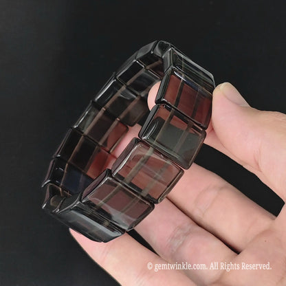 Angle view of natural ice obsidian rectangular plate bead bracelet held in hand showcasing internal light transmission