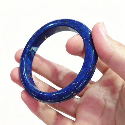 Fingers holding a smooth solid natural lapis lazuli bangle displaying deep royal blue color with golden pyrite flecks