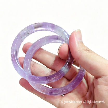 Pair of light purple natural amethyst bangles held in hand showing pastel crystal clarity