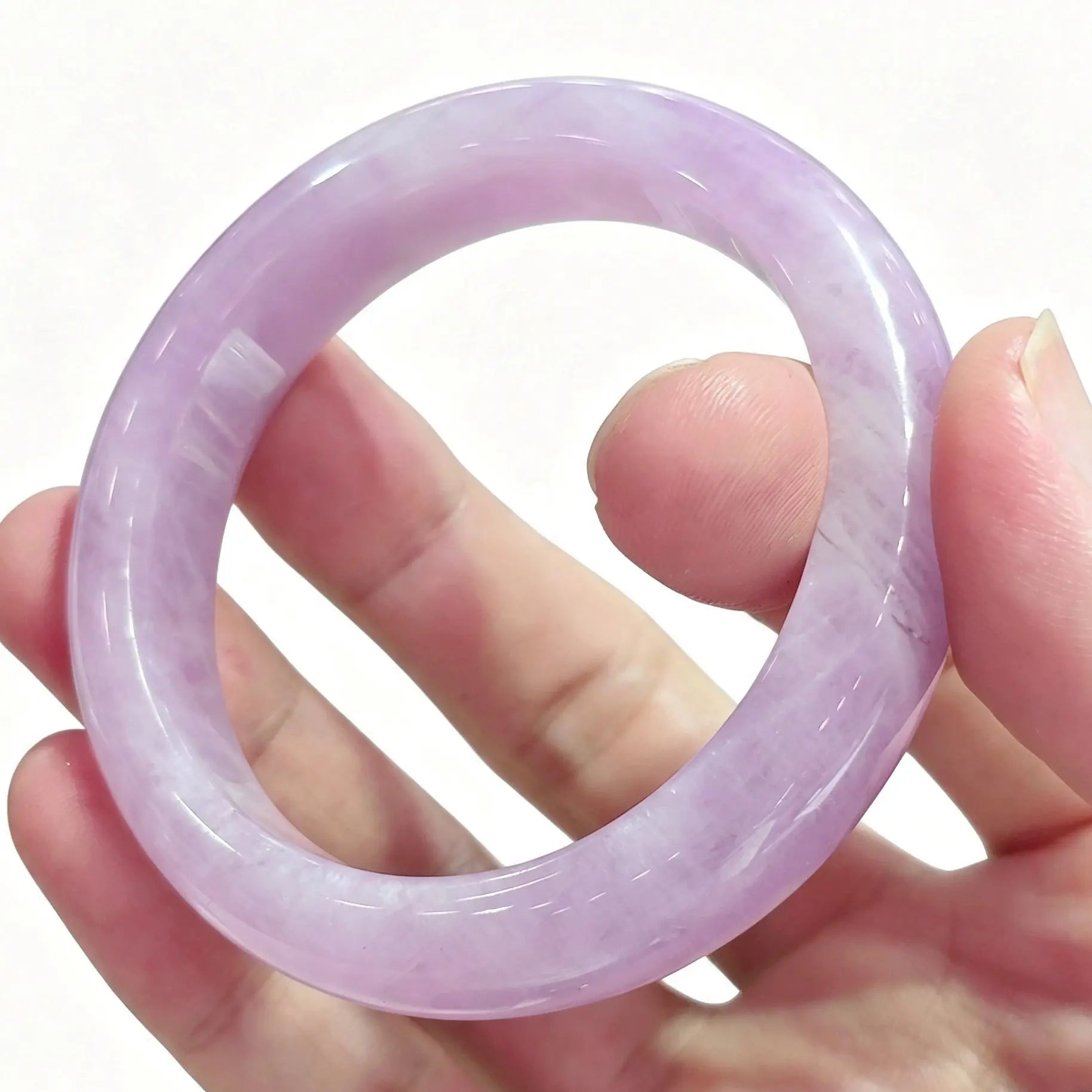 Fingers holding a smooth solid natural lavender kunzite crystal bangle displaying soft pastel purple color against light background