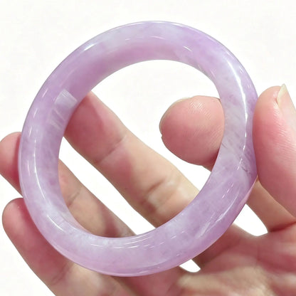 Fingers holding a smooth solid natural lavender kunzite crystal bangle displaying soft pastel purple color against light background