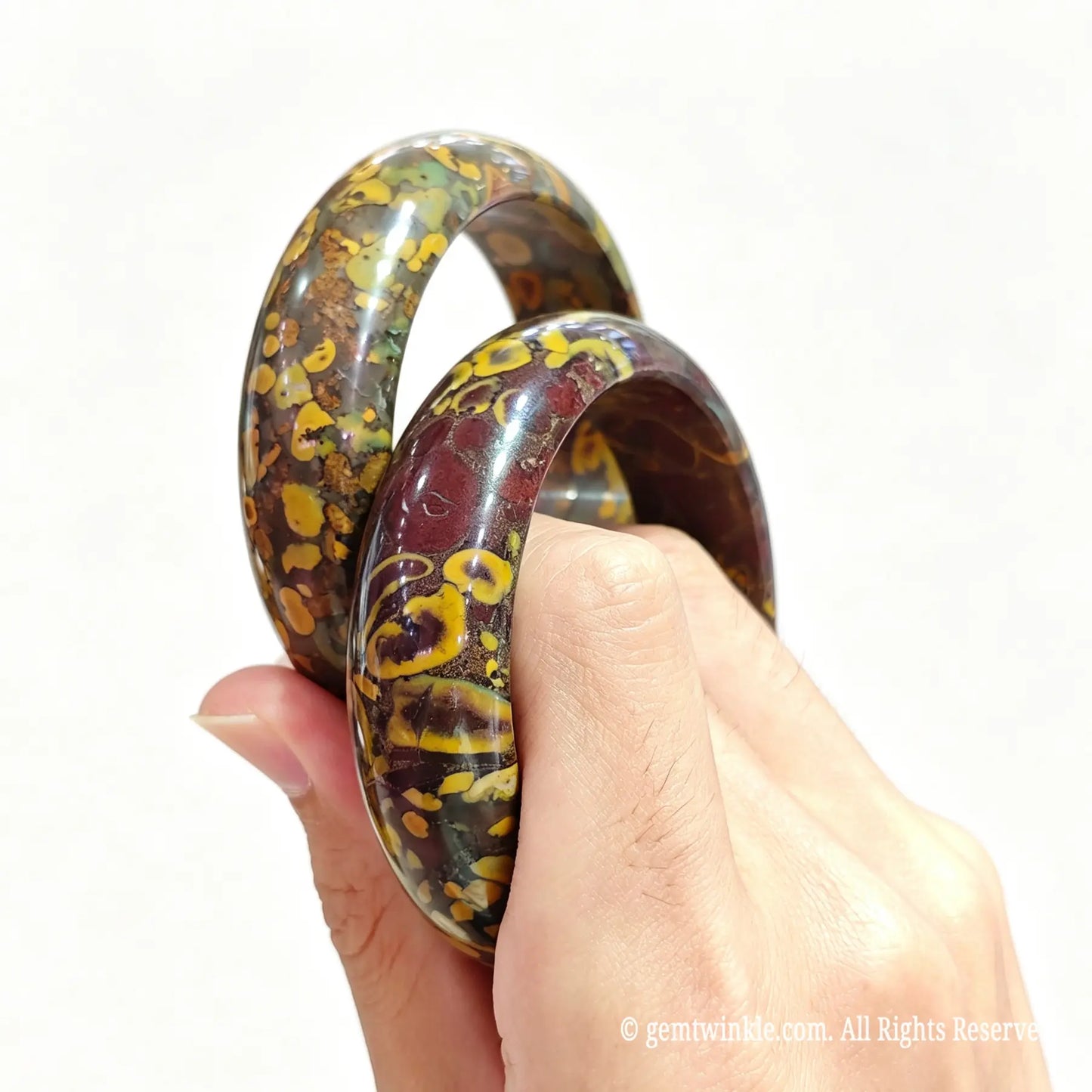 Pair of natural nuwa stone bangles held in hand showing earth-toned brown and yellow spotted mineral textures