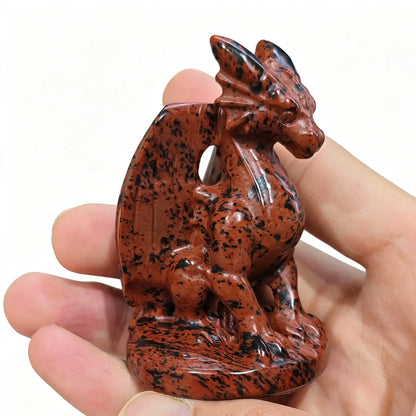 Natural mahogany obsidian dragon statue 7cm height held in hand showing reddish brown mottled texture and winged dragon side profile