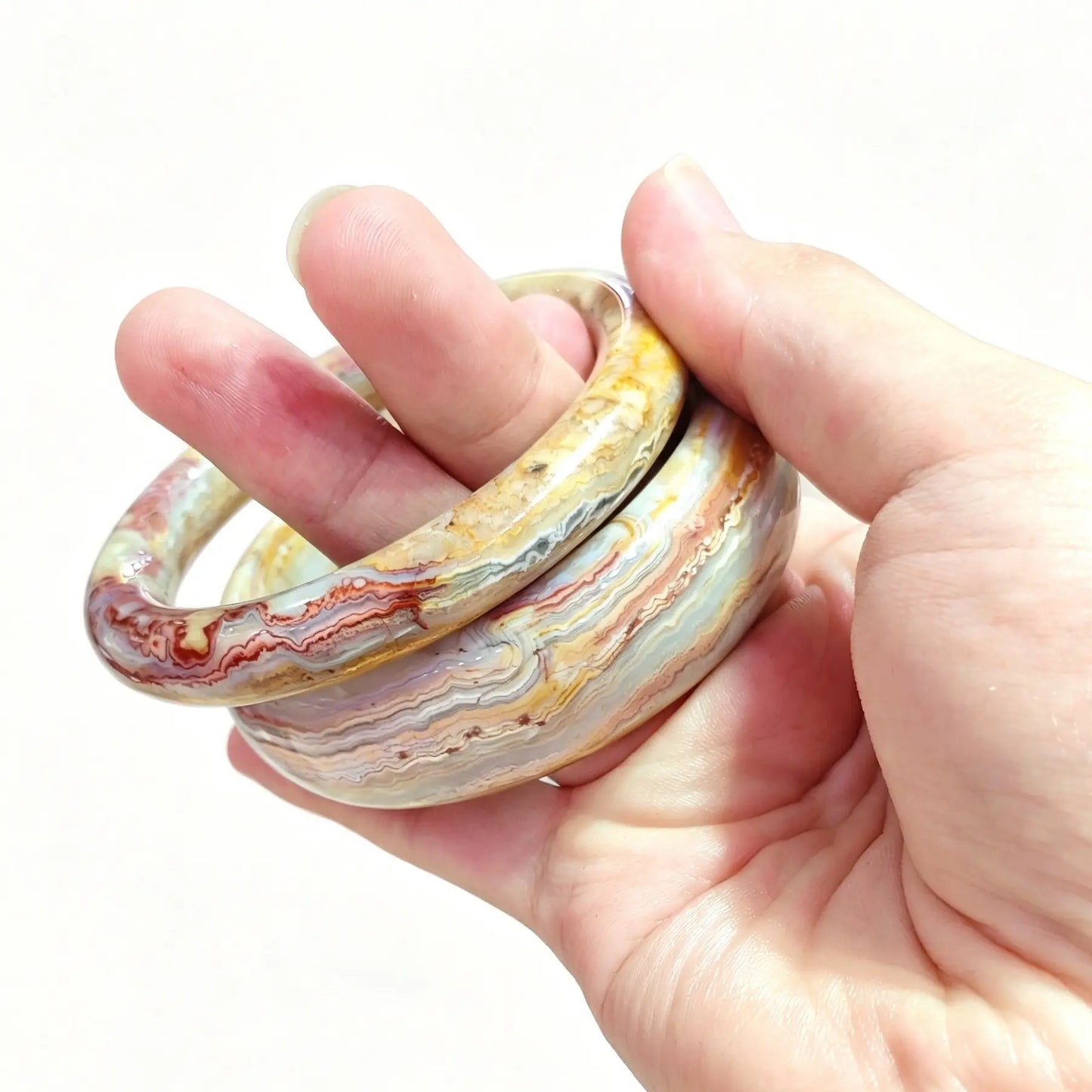 Two natural mexican crazy lace agate bangles held in hand for boutique stock selection