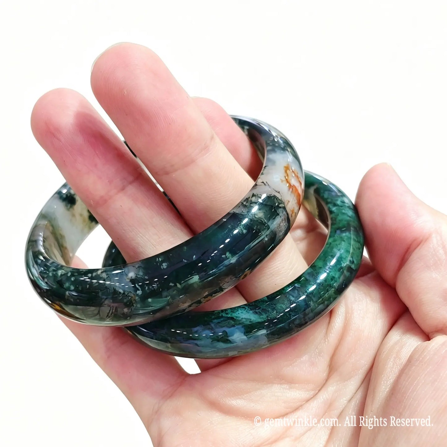 Pair of natural moss agate bangles held in hand showing botanical green filaments