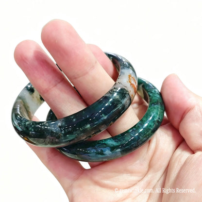Pair of natural moss agate bangles held in hand showing botanical green filaments