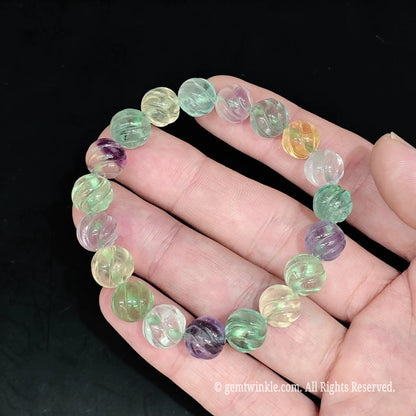 Full view of natural multi color fluorite pumpkin carved bead bracelet resting open on hand showing pastel gemstone mix
