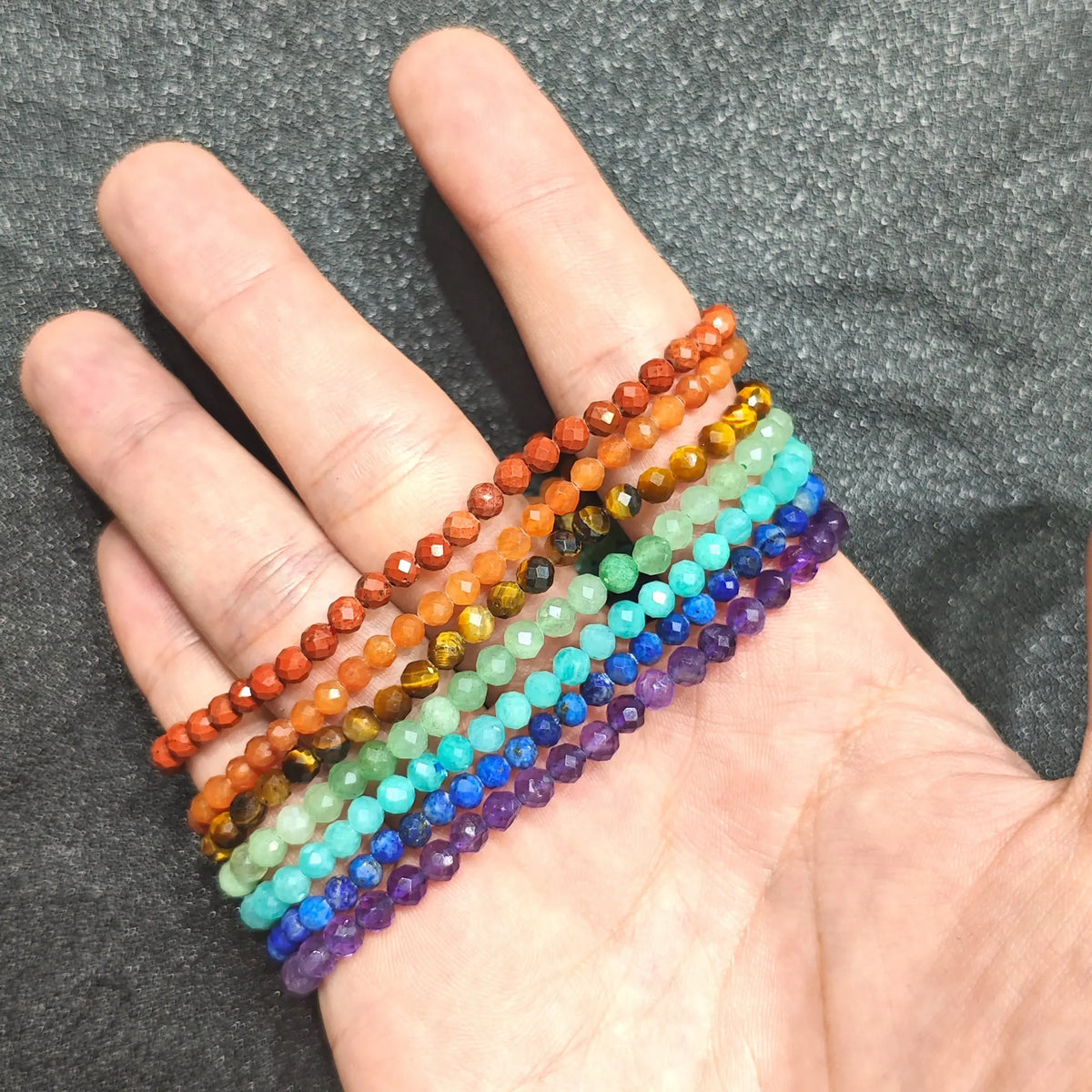 set of 7 natural multi gemstone faceted bead stretch bracelets displayed flat on open hand showing rainbow color spectrum