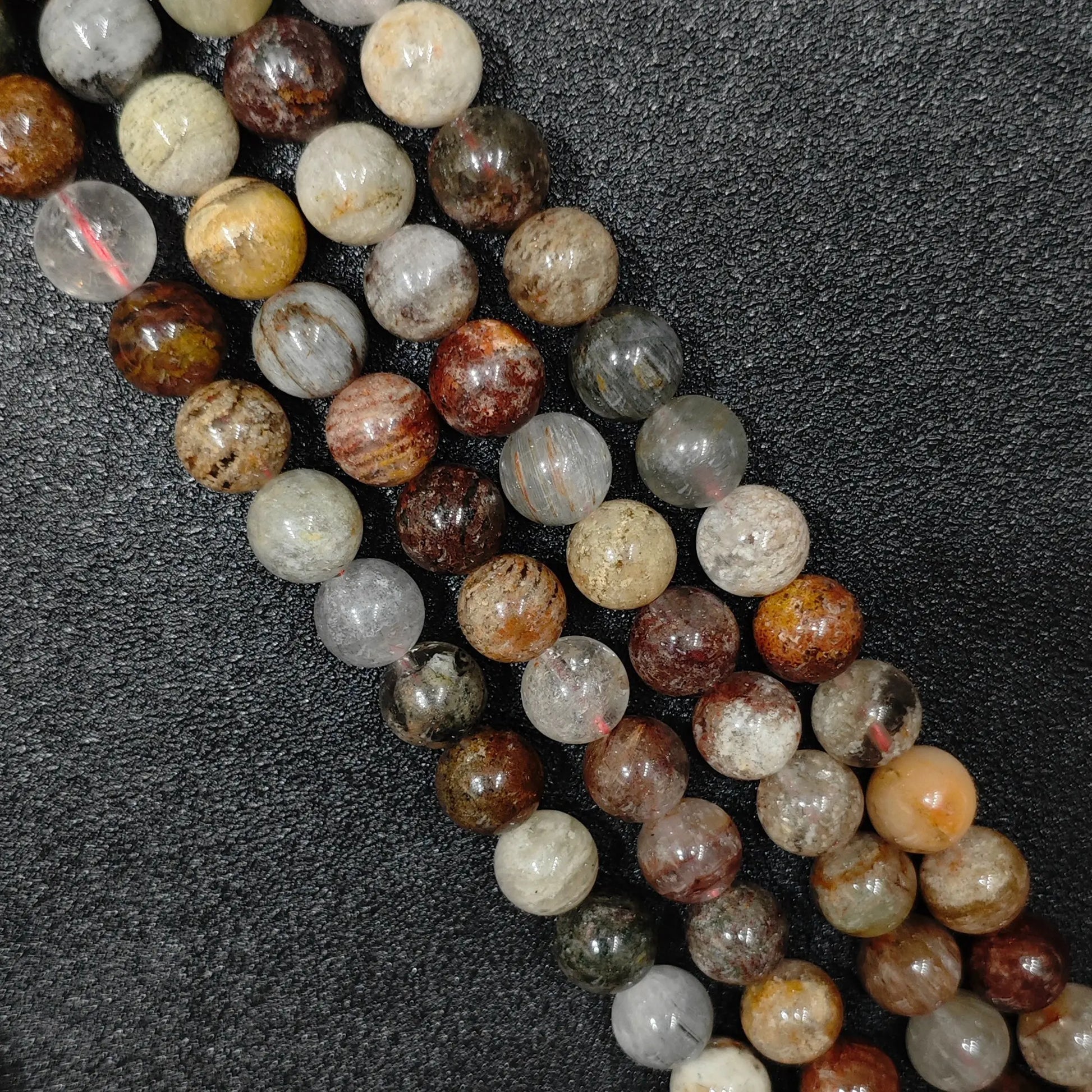 close look at 10mm natural multi color phantom quartz gemstone strands with rich scenic lodolite inclusions on black background
