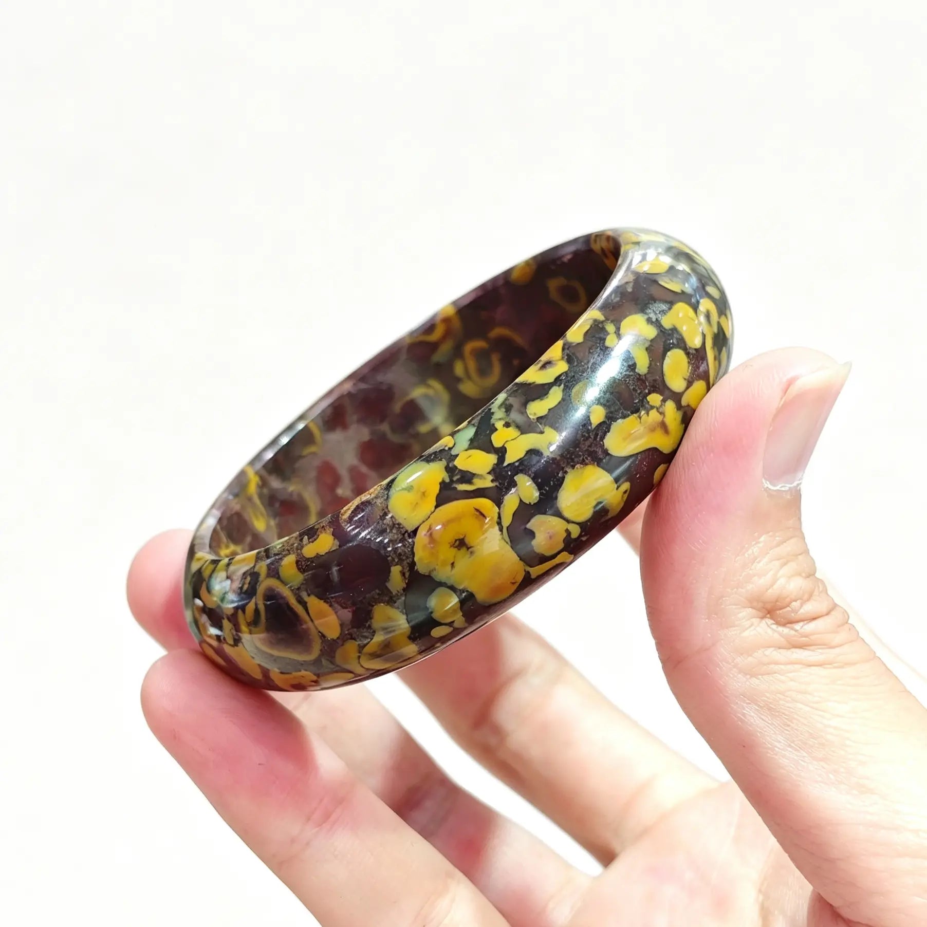 Hand holding a natural nuwa stone bangle showcasing rich leopard skin jasper orbicular patterns and high polish