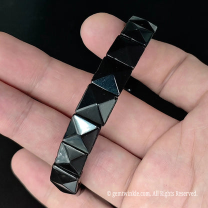 Side angle view of natural obsidian 3d pyramid faceted square bead bracelet held in hand highlighting sharp facet angles
