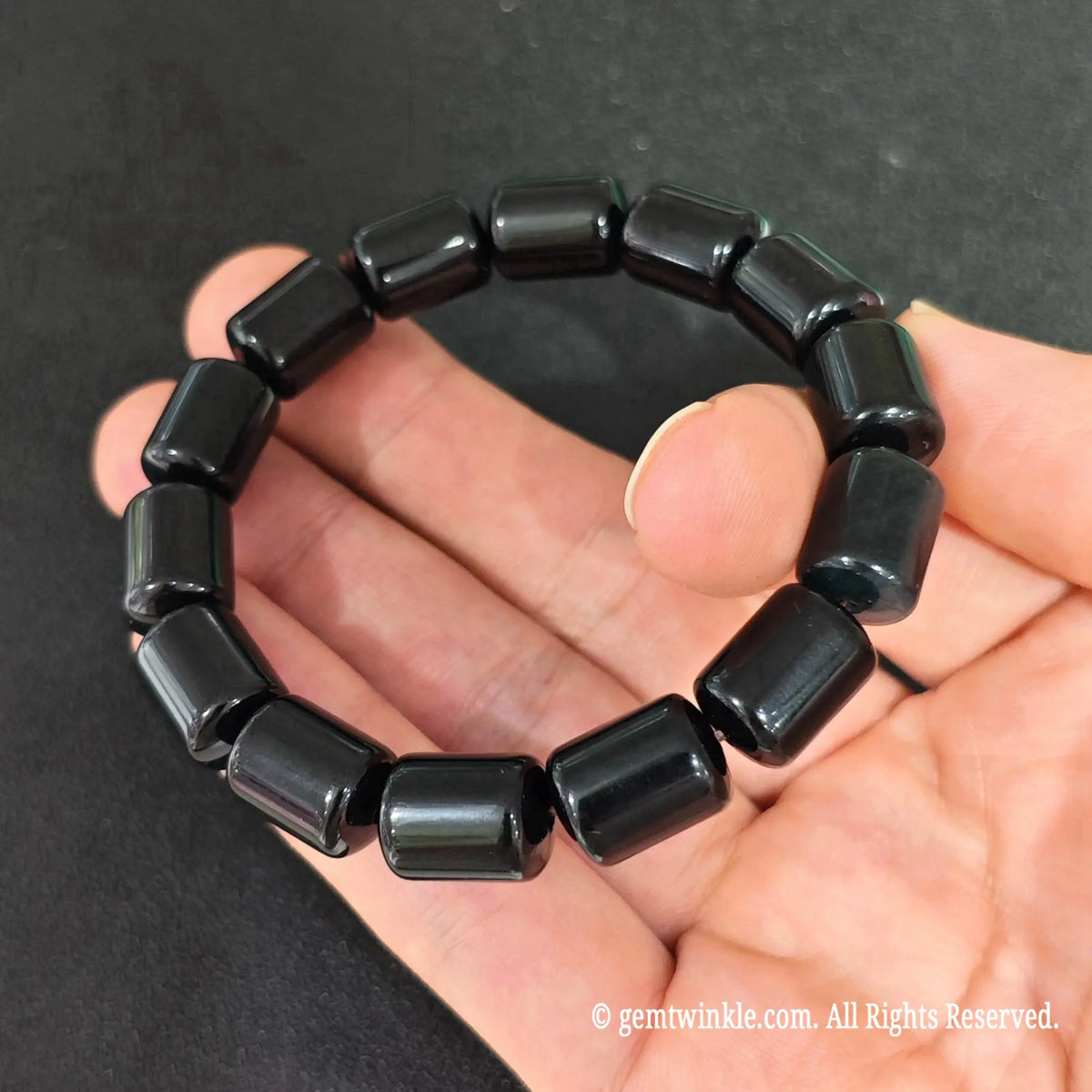 natural black obsidian barrel bead elastic bracelet worn on wrist against dark background