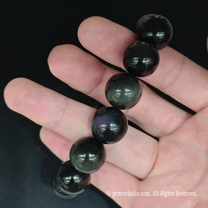 Natural obsidian beads string held under studio lighting displaying iridescent purple and green sheen eyes
