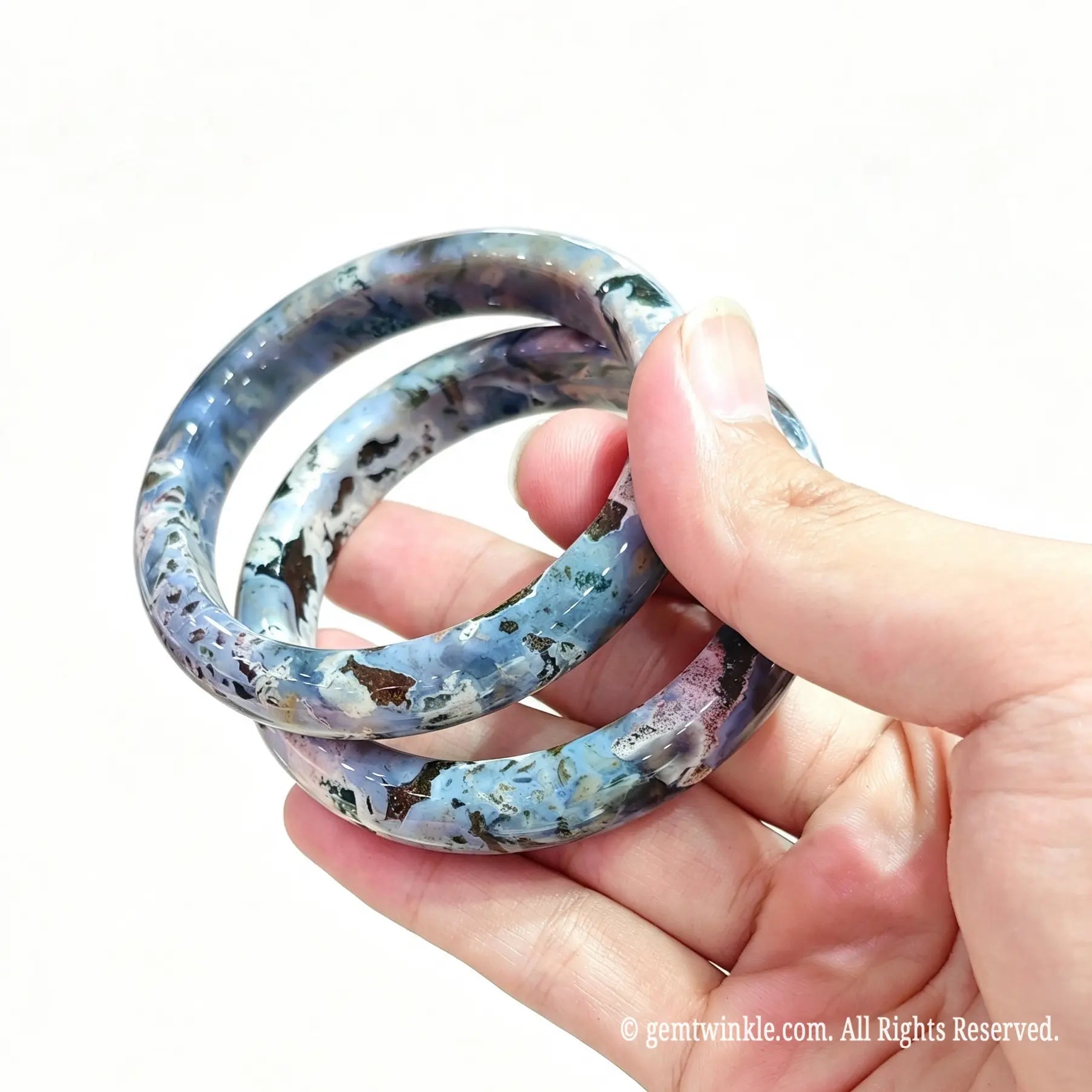 Hand displaying two natural ocean jasper bangles with rich mineral swirls and orbicular eyes
