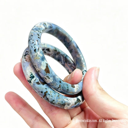 Pair of natural ocean jasper bangles held in hand showing intricate mineral orb swirls