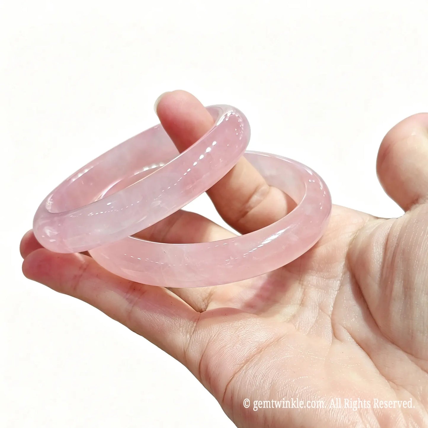Pair of natural rose quartz bangles held in hand showing smooth polish and delicate translucent structure