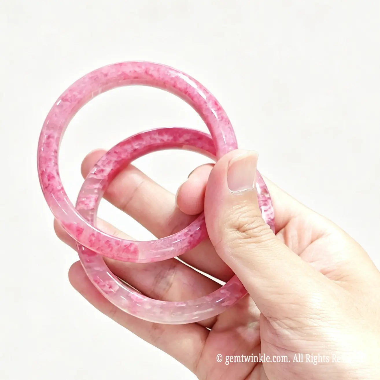 Pair of natural rose rhodonite bangles held in hand showing fine polish and characteristic mineral patterning