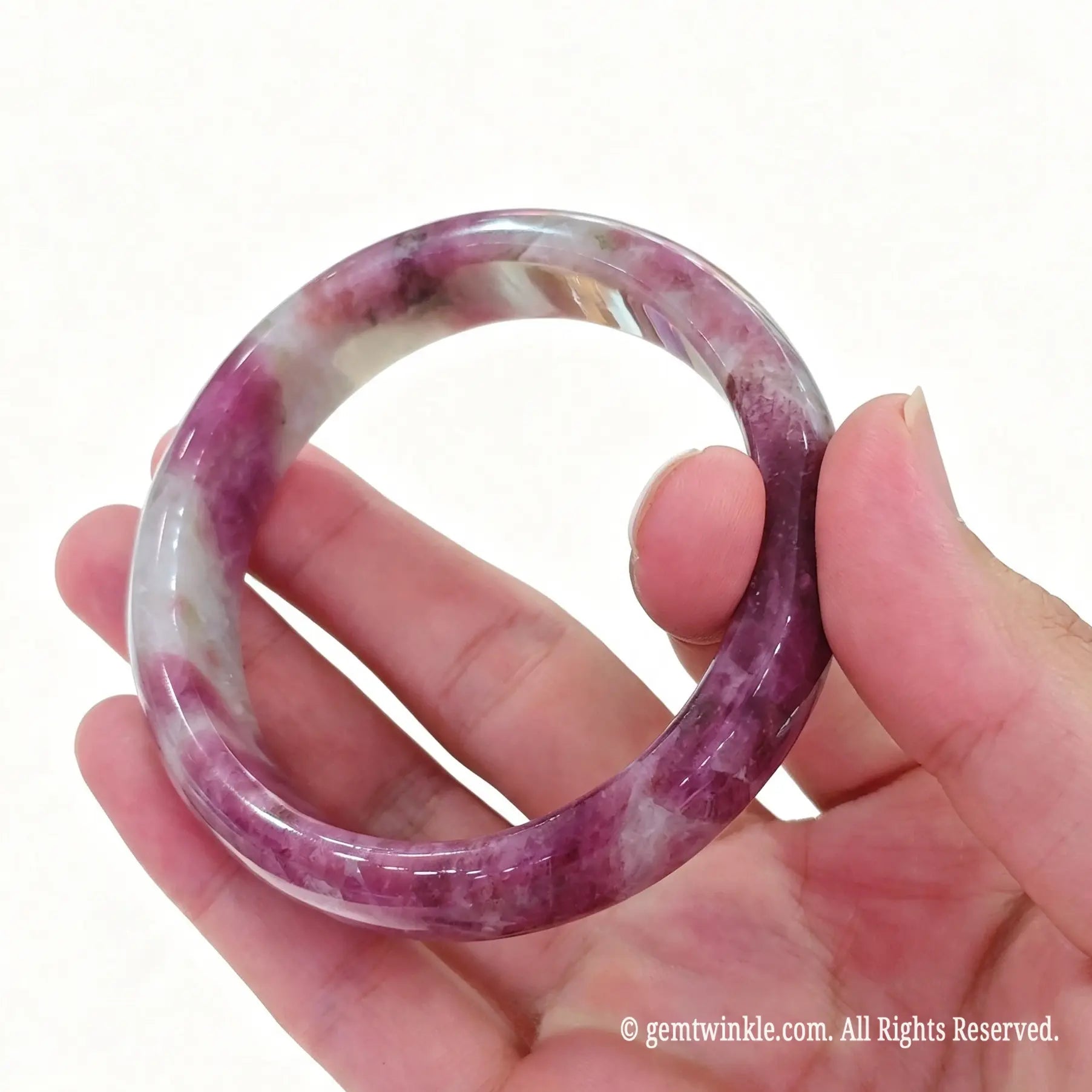 Single natural plum blossom tourmaline bangle held up to show rose pink mineral contrast and smooth polish